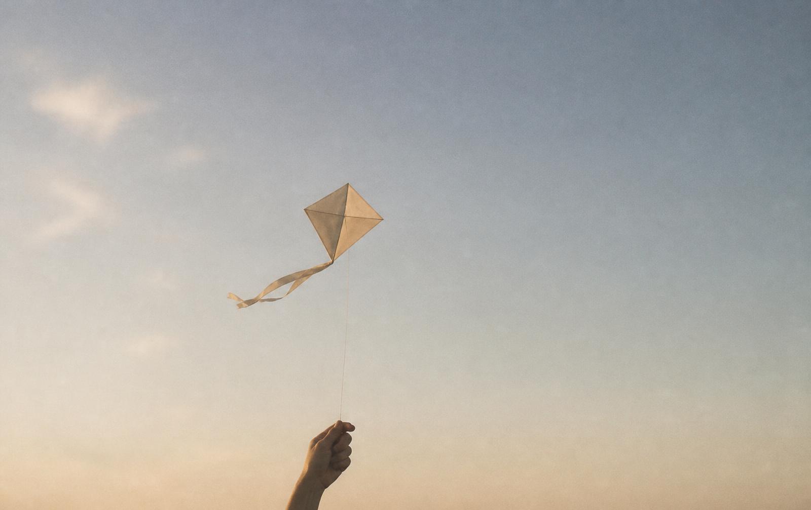 Una cometa de papel sostenida por un hilo contra un cielo amplio al atardecer